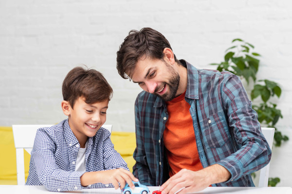An adult and child play with toy cars at a table